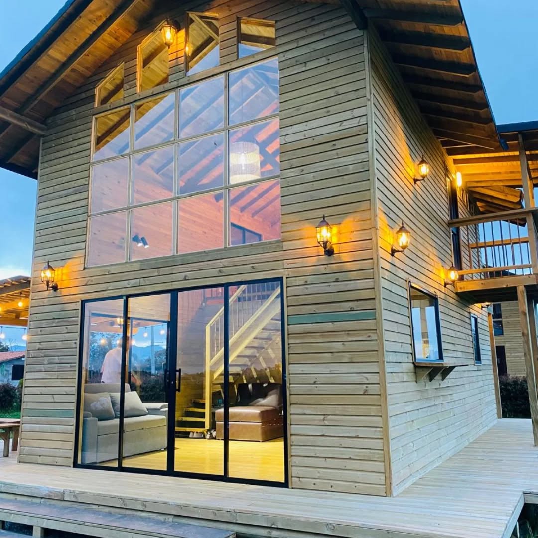 Cabaña en madera con ventanales y deck iluminado